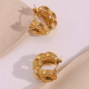 Close-up of chunky gold-plated chain link earrings on a textured stone surface with water drops