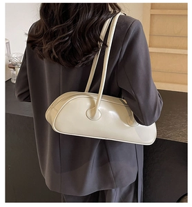 Model wearing a large cream shoulder bag in soft leather with a minimalist long shape