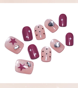 Close-up of pink cat-eye press-on nails with red stars, black dots and silver heart charms