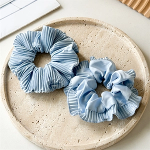 Detail of light blue pleated and ruffled satin scrunchies set on a minimalist tray