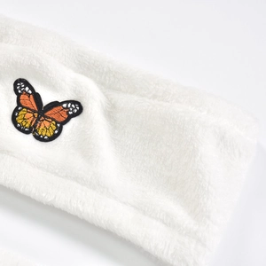 Détail d'un bandeau en peluche blanche avec broderie papillon orange et texture très douce