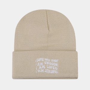 Close-up of beige knitted beanie with I AM ENOUGH embroidery detail and ribbed texture