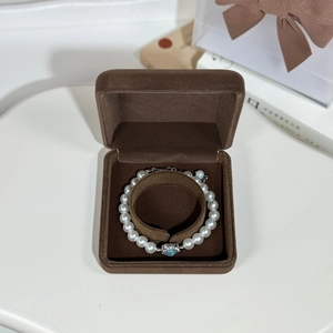 Detail of a pearl bracelet with blue heart pendant in a plush brown velvet jewelry box