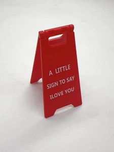 Close-up of red mini folding sign with A LITTLE SIGN TO SAY I LOVE YOU text print