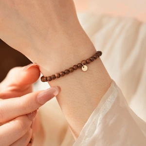 Close-up of minimalist dark wood bead bracelet with a gold charm on a model wrist