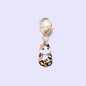 Detail of a cute calico cat enamel pendant with a golden heart-shaped lobster clasp