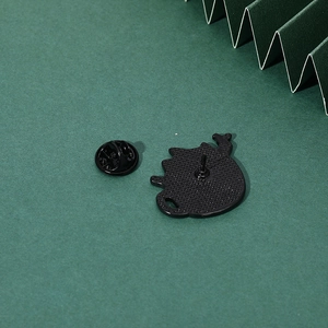 Detailed back view of black enamel kitten brooch with rubber clutch on green paper