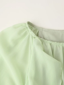 Close-up of the pleated round neckline on a light green chiffon dress with soft textures
