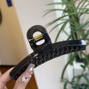Close-up of a large black glossy hair claw clip with a strong golden metal spring