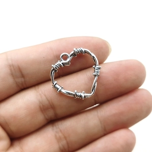 Antique silver thorn heart pendant held by fingers, ideal for DIY jewelry making crafts