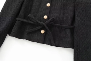 Close-up of black tweed jacket featuring textured weave and decorative gold buttons