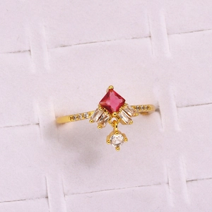 Detailed view of a gold flower ring with a red gemstone and a dangling zircon pendant