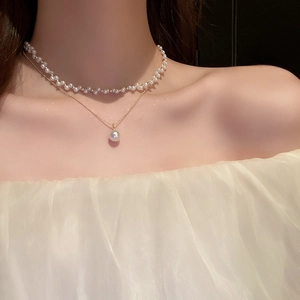 Détail d'un collier de perles double couche avec chaîne dorée et grand pendentif perle