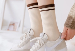 Close-up of beige cotton crew socks with brown striped cuffs worn with sneakers
