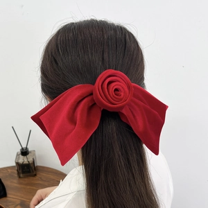 Détail d'une grande pince à cheveux en velours rouge avec rose, portée à l'arrière