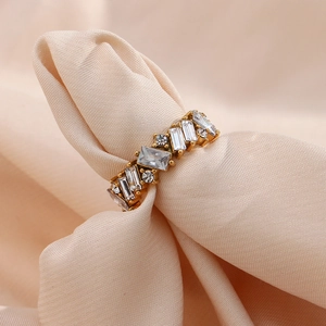 Macro detail of gold ring with clear rectangular and round zircon stones on beige satin