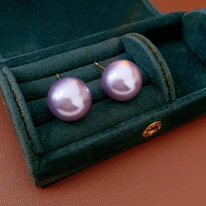 Detail of purple pearl stud earrings presented in a luxury green velvet jewelry box