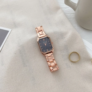 Detailed view of women's rectangular rose gold watch with grey dial on linen background