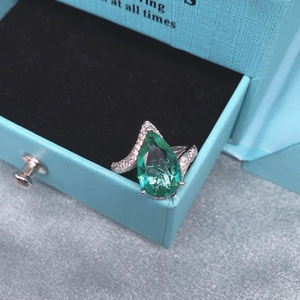 Macro shot of a pear-cut green gemstone ring with wavy sparkling diamond band details