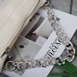 Bolso beige con una llamativa cadena de aluminio plateado en un entorno de estilo