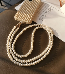 Detail of beaded white pearl phone lanyard with gold metal clasp on beige case