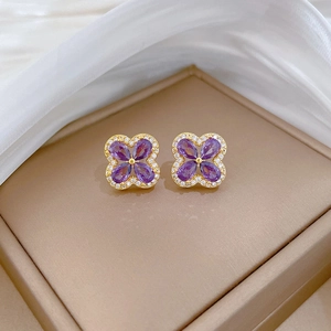 Close-up of gold-plated clover earrings with purple gems and zircon accents on beige box