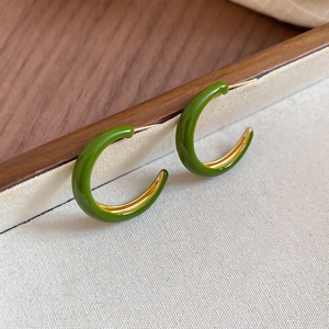 Macro shot of vintage C-shape earrings with dark green enamel and golden metal finish