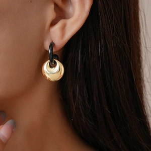 Detail of geometric round earrings in gold and black on model showing elegant metallic texture