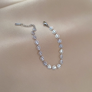Minimalist silver smiley face link chain bracelet in stainless steel on beige background