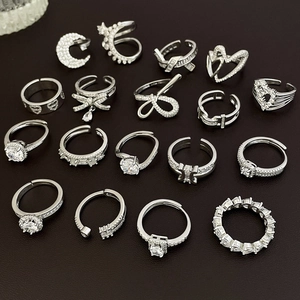 Flat lay of multiple silver rings with zircon bows and hearts on a brown leather texture
