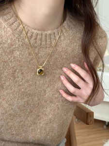 Macro shot of a square tiger eye stone pendant on a gold necklace over a brown knit sweater