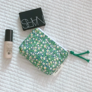 Flat lay of a floral cotton mini pouch with zipper and green tassel for makeup storage