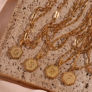 Detailed close-up of golden paperclip layered necklace with hexagonal letter pendants