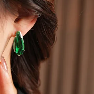 Elegant teardrop-shaped green zircon earrings with silver pins on a female model