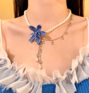Detailed view of a French style necklace featuring a blue beaded flower and elegant pearls