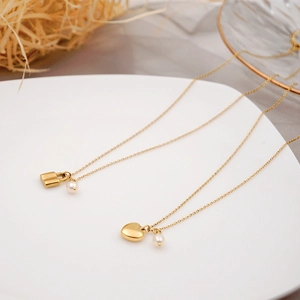 Colliers dorés avec pendentifs cœur et cadenas et perles sur assiette blanche