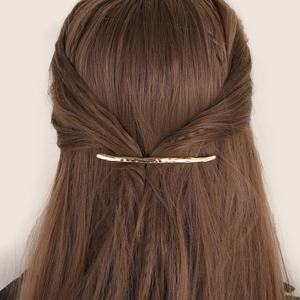 Minimalist gold metal hair clip with irregular hammered texture on long brown hair
