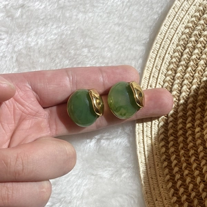 Green oval resin earrings with gold wavy metal trim shown held by hand on a white rug