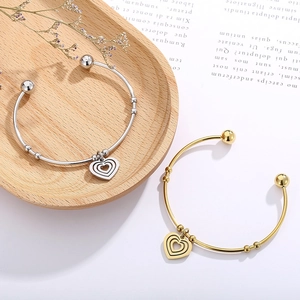 Detailed view of layered gold and silver heart pendants on open cuff bracelets