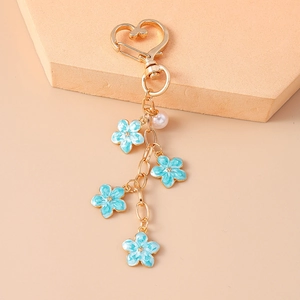 Detail of blue enamel flowers and pearl pendant on a gold heart keychain for bags