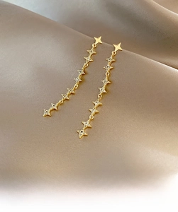 Macro shot of long gold star tassel earrings with zircons on elegant champagne satin