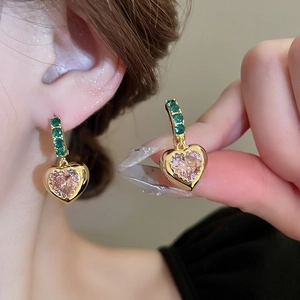 Retro gold heart earrings with green and pink gemstones shown on model and hand