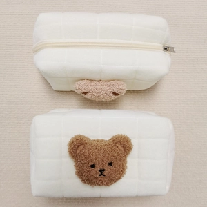 Detailed macro view of white quilted plush makeup bag with brown bear embroidery