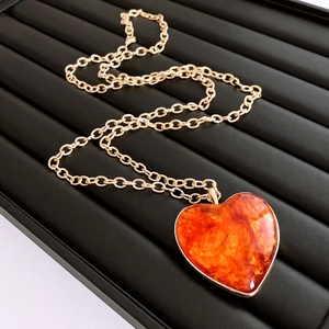 Detail of heart pendant with orange marble texture and gold chain on leather stand