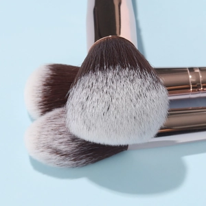 Detail of three soft synthetic brushes with rose gold ferrules on light blue surface