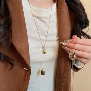 Detail of 18k gold-plated teardrop pendant Y-necklace worn on white and brown clothing