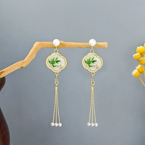 Detail of long gold tassel earrings with bamboo pattern and white pearls on wooden branch