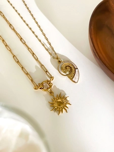 Macro shot of gold paperclip chain with sunburst and seashell shell pendants