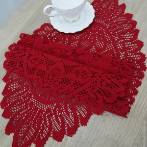 Red crochet lace Christmas table runner on wooden surface with white tea set decor