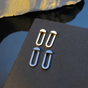 Dettaglio di orecchini geometrici in oro e argento su un supporto espositivo nero